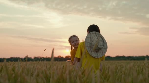 Uma mãe agricultora gentil com uma criança em um campo com trigo ao pôr-do-sol, cultivando grãos para fazer pão, uma criança feliz, um negócio familiar em um rancho, examinando as culturas cultivadas com um bebê em seus braços - Filmagem, Vídeo
