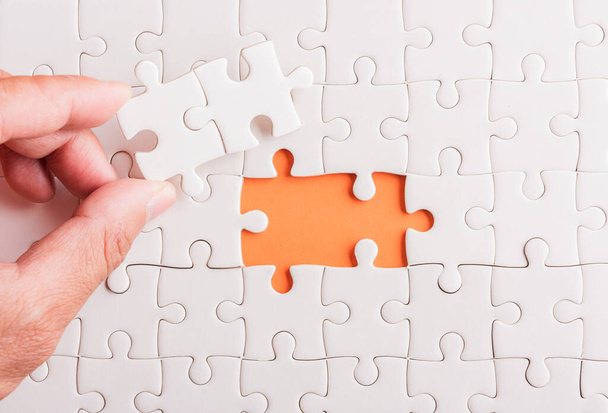 Top view flat lay of hand-holding last piece white paper jigsaw puzzle game last pieces put to place for solve problem complete mission, studio shot on an orange background, quiz calculation concept - Photo, image