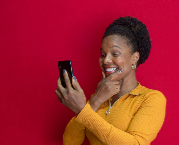 fekete nő mosolyog és gondolkodás gazdaság egy tabletta sárga ing piros háttér - Fotó, kép