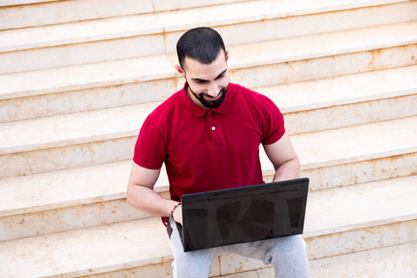 Arabic man using laptop outside and sitting on stairs - Фото, изображение