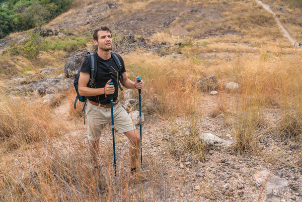 caucasian backpack hiker with trekking stick walking on trekking trail in dry meadow on rocky hill on mountain in summer for sport leisure - Φωτογραφία, εικόνα