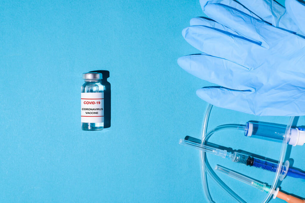 Vial of anti-covid vaccine, medical gloves, syringe with injection on blue background, flat lay. Vaccination concept. - Photo, Image