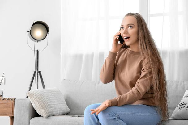 Happy young woman talking by mobile phone at home - Φωτογραφία, εικόνα