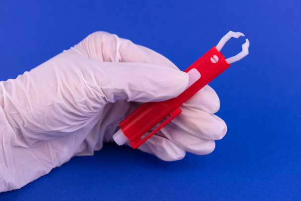 Tick εργαλείο αφαίρεσης στο χέρι ενός γιατρού σε μπλε φόντο - Φωτογραφία, εικόνα