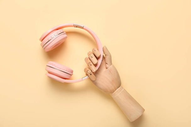 Mão de madeira com fones de ouvido modernos no fundo de cor - Foto, Imagem