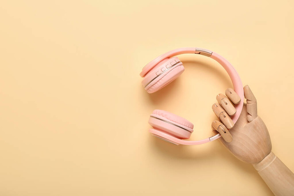 Wooden hand with modern headphones on color background - Photo, Image