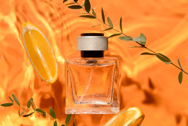 Botella de perfume, ramas anaranjadas y verdes en agua sobre fondo de color, primer plano - Foto, imagen