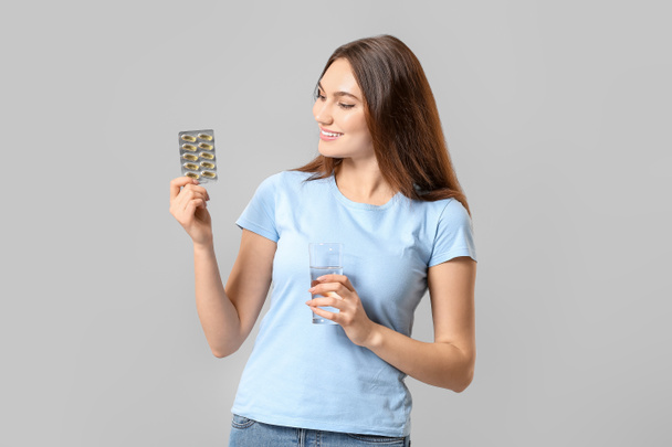 Mujer joven con píldoras de aceite de pescado sobre fondo claro - Foto, Imagen