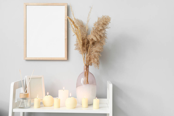 Полка с горящими свечами и вазой возле светлой стены - Фото, изображение