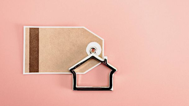The concept of mortgage, sale and rental of housing and real estate. Mortgage credit lending. A tag or sticker with a keychain in the form of a house on a pink background. Copy space. Mock-up - Photo, Image