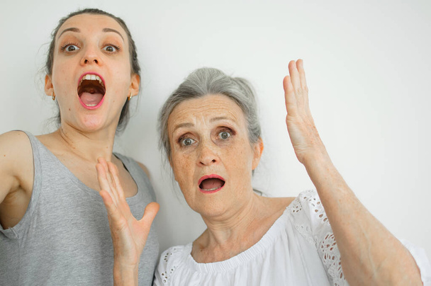 Emotional adult daughter with her senior moter are screaming and looking at the camera, crazy family of different age generations having fun on white background, mothers day - Photo, Image