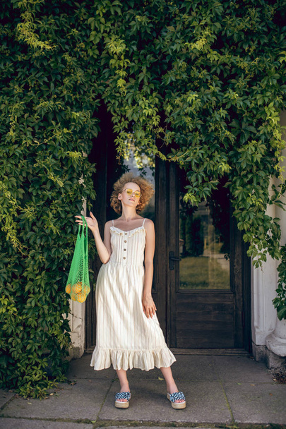 Young woman in a white long dress holding a green mesh bag in her hands - Foto, immagini