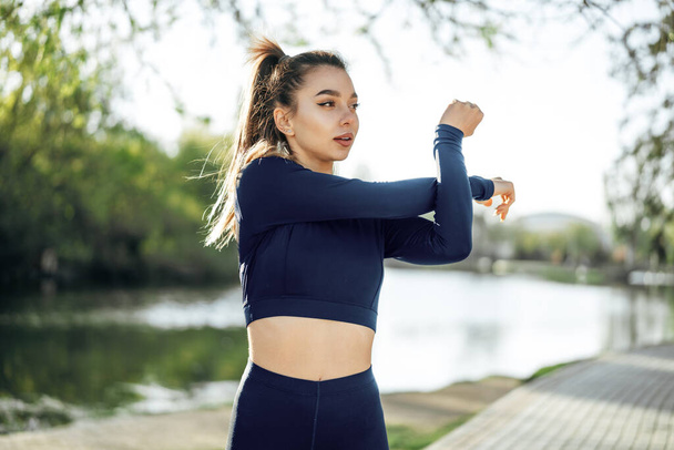 Fit young girl in dark blue sportswear exercising in park - 写真・画像