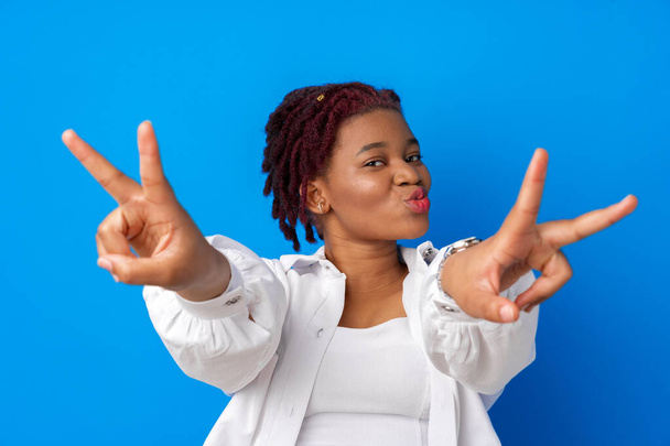 Beautiful young afro woman showing victory sign against blue background - Фото, изображение