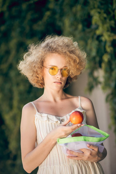 A picture of a woman in a light dress with a nectarine in her hand - Foto, Bild
