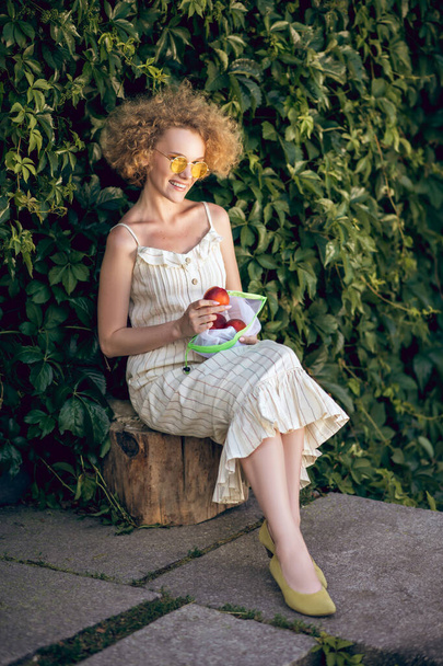 gekrulde jonge vrouw met nectarines op zoek gelukkig - Foto, afbeelding