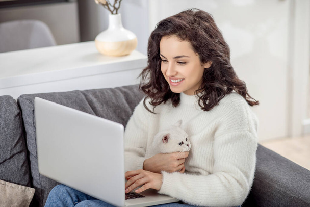 Dark-haired woman working on a laptop and hugging her cat - Φωτογραφία, εικόνα