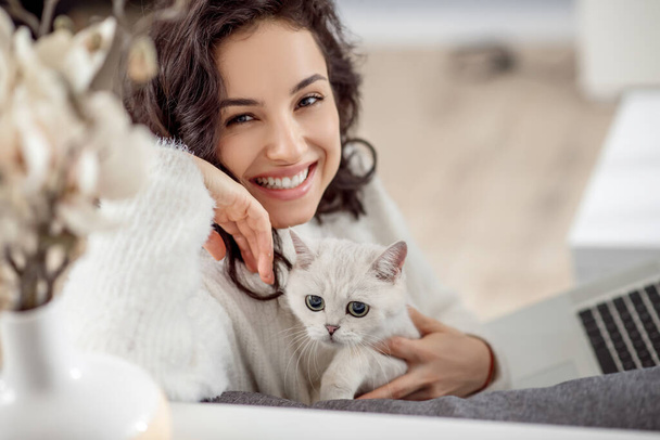 Cute young woman holding a white cat and smiling nicely - Photo, Image