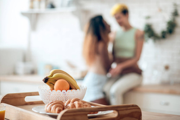 Fruits and croissants on tray and girlfriends at distance - Fotoğraf, Görsel