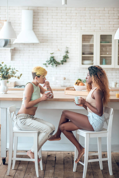 Two pretty girlfriends drinking coffee at kitchen table - Zdjęcie, obraz