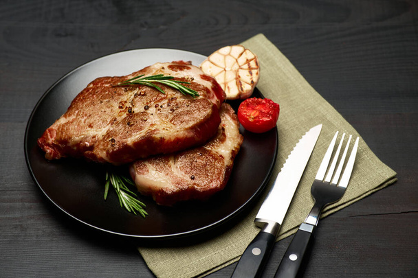 Grilled roated beef steaks on black ceramic plate - Fotó, kép