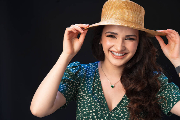 Beautiful young woman with straw hat posing against black background - Zdjęcie, obraz