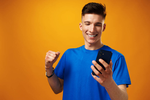 Nuori mies käyttää älypuhelinta keltaista taustaa vasten - Valokuva, kuva