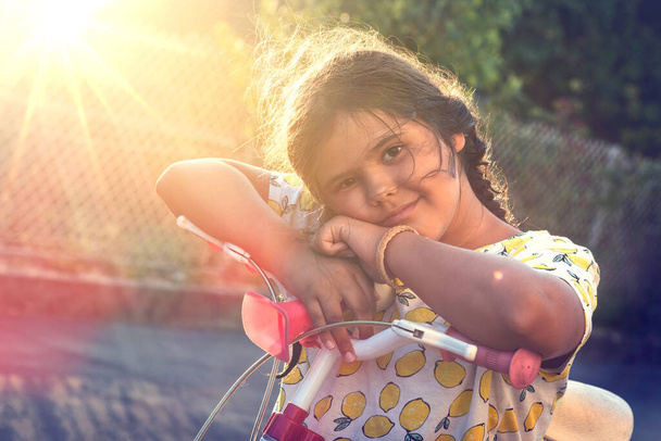 Szczęśliwa młoda dziewczyna pozowanie w rowerze na zewnątrz o zachodzie słońca - Zdjęcie, obraz