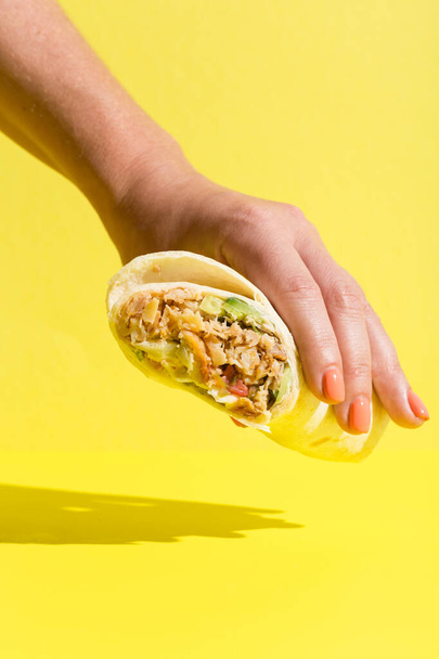 Hand takes doner roll shawarma with chicken and vegetables on yellow - Fotografie, Obrázek