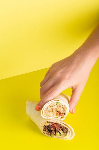 Hand takes doner roll shawarma with chicken and vegetables on yellow - Foto, afbeelding