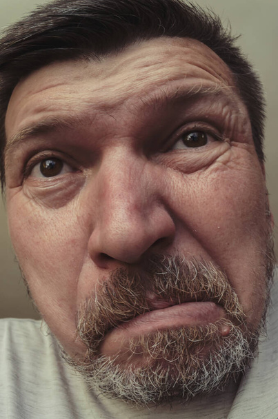 Unusual portrait of a bearded man with short brown hair. A grown man with gray stubble makes faces. Grimaces in front of the camera - Photo, Image