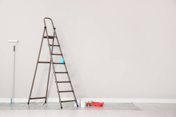 Decorator's tools and ladder near white wall indoors, space for text - Foto, Bild