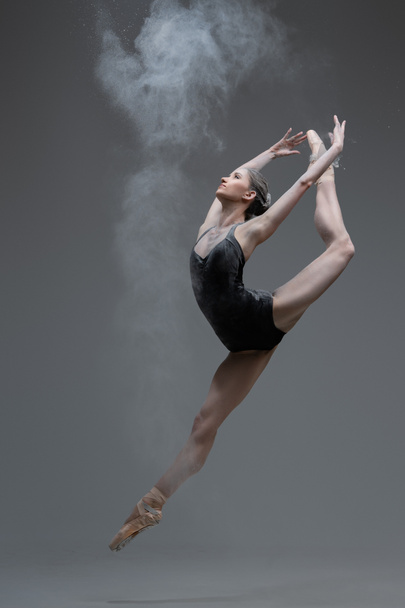 Skilled ballerina dancing leaping against gray background - Фото, изображение