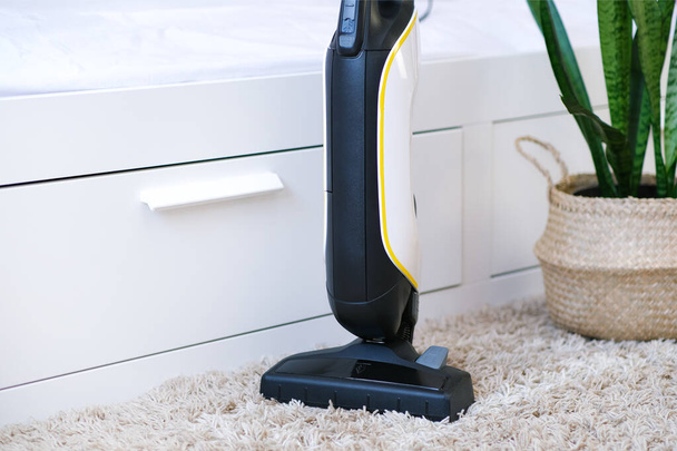 cordless vacuum cleaner is used to clean the carpet in the room. Housework with a new handheld vacuum cleaner. House cleaning, care and technology concept. - 写真・画像