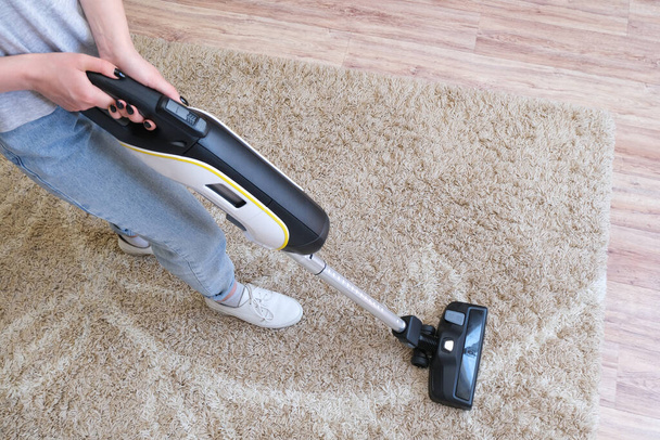 cordless vacuum cleaner is used to clean the carpet in the room. Housework with a new handheld vacuum cleaner. House cleaning, care and technology concept. - 写真・画像