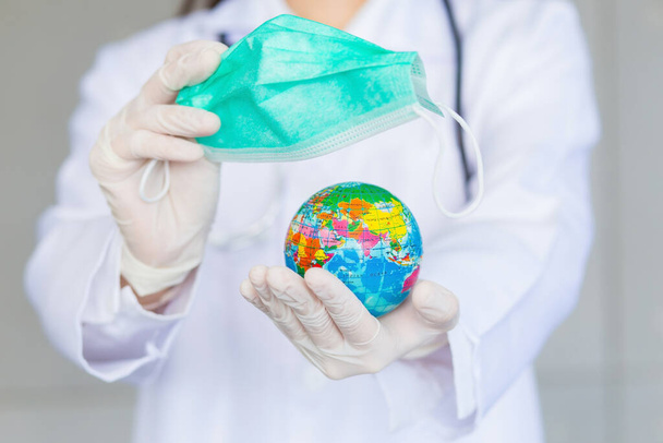 Asijské žena lékař drží globální míč a lékařskou masku obličeje jako znamení zachránit svět a nový normální životní styl téma. - Fotografie, Obrázek