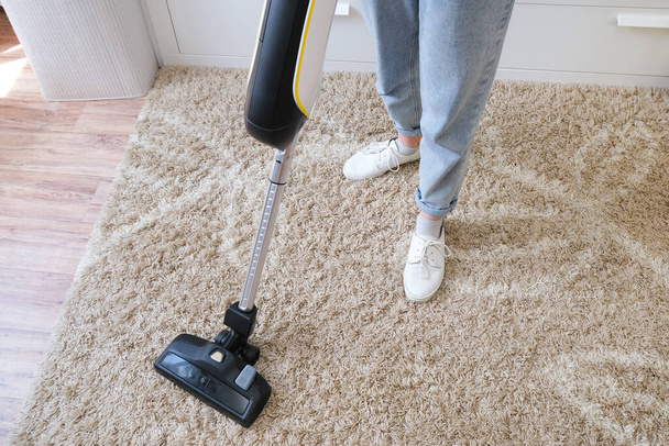 cordless vacuum cleaner is used to clean the carpet in the room. Housework with a new handheld vacuum cleaner. House cleaning, care and technology concept. - Foto, afbeelding