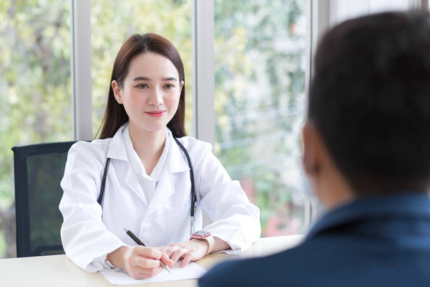 Asian professional  woman doctor who wears medical coat talks with a man patient to consult and suggest healthcare information to him. - Photo, Image