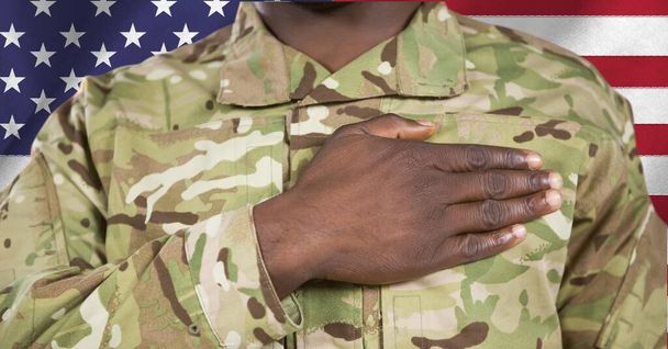 Composition of midsection of male soldier with hand on heart, against american flag. patriotism, independence and military concept digitally generated image. - Фото, изображение