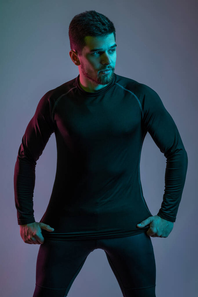 Young man in black sportswear confidently posing in studio - Zdjęcie, obraz