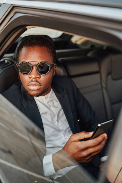 Cool african businessperson with phone sitting inside of car - Photo, Image