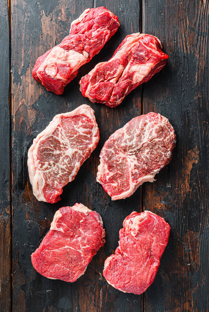 Variety of fresh Black Angus Prime raw beef steakes on old rustic dark wooden background, top view - Foto, afbeelding