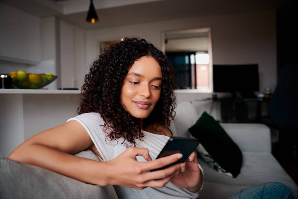 Mixed race African-American female relaxing on couch texting on cellular device  - Photo, Image