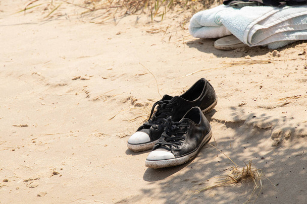 чорні кросівки стоять на піску біля моря на сонці, мода дозвілля, кросівки
 - Фото, зображення