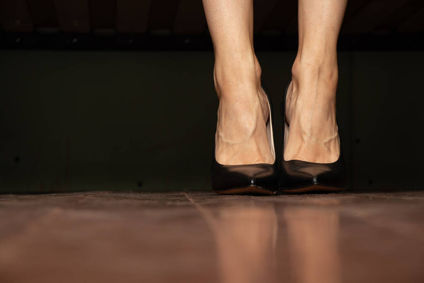 κορίτσι με μαύρα ψηλοτάκουνα παπούτσια στέκεται σε ένα ξύλινο παλιό πάτωμα στο σπίτι, πόδια στο πάτωμα, γυναικεία παπούτσια - Φωτογραφία, εικόνα