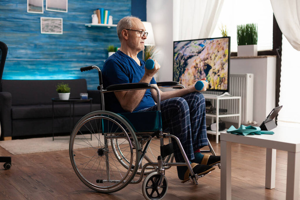 Tekerlekli sandalyede oturmuş, tablet bilgisayardan spor videosu seyrediyor. - Fotoğraf, Görsel