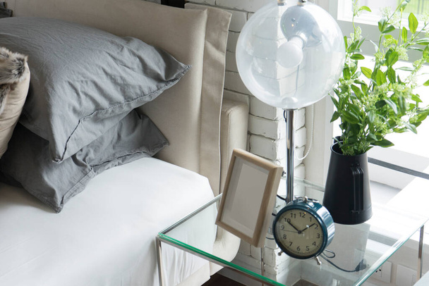 сучасна лампа, фоторамка і годинник на столі біля ліжка
 - Фото, зображення