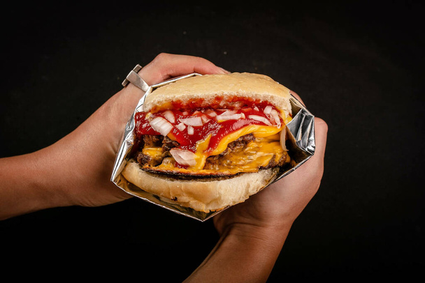 A closeup shot of a male hand holding a hamburger on an isolated black background - Foto, Imagen