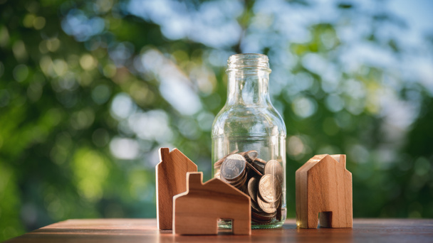Holzhäuser und ein Glas mit Münzen. Das Konzept des Hauskaufs, der Miete und der Besteuerung von Immobiliengeschäften. mit natürlichem grünen Hintergrund - Foto, Bild