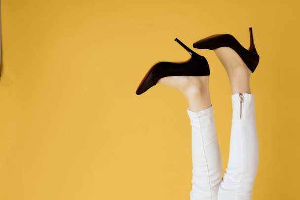 ανάποδη γυναικεία πόδια σε μαύρα παπούτσια με κίτρινο φόντο - Φωτογραφία, εικόνα